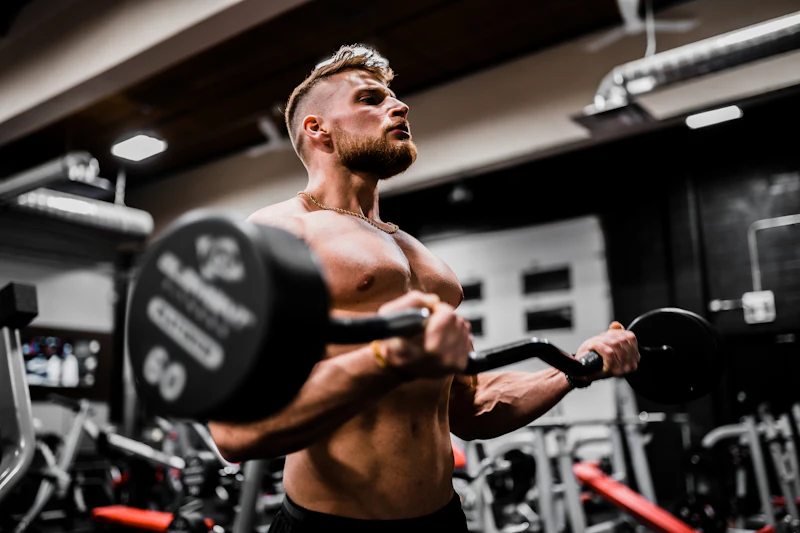 Athlète musclé réalisant un curl à la barre en salle de sport